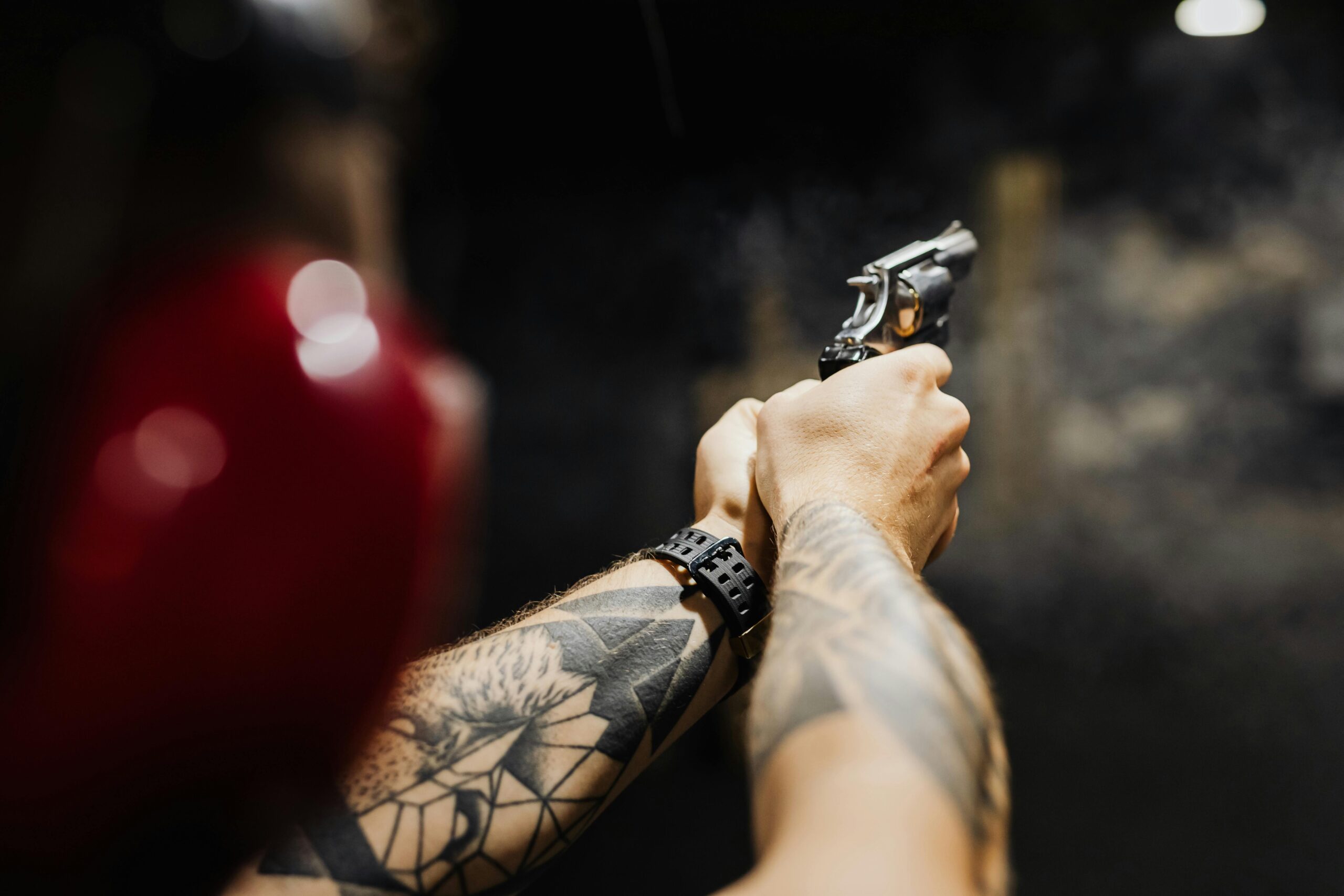 A focused close-up shot of tattooed arms holding a revolver in a dark setting.